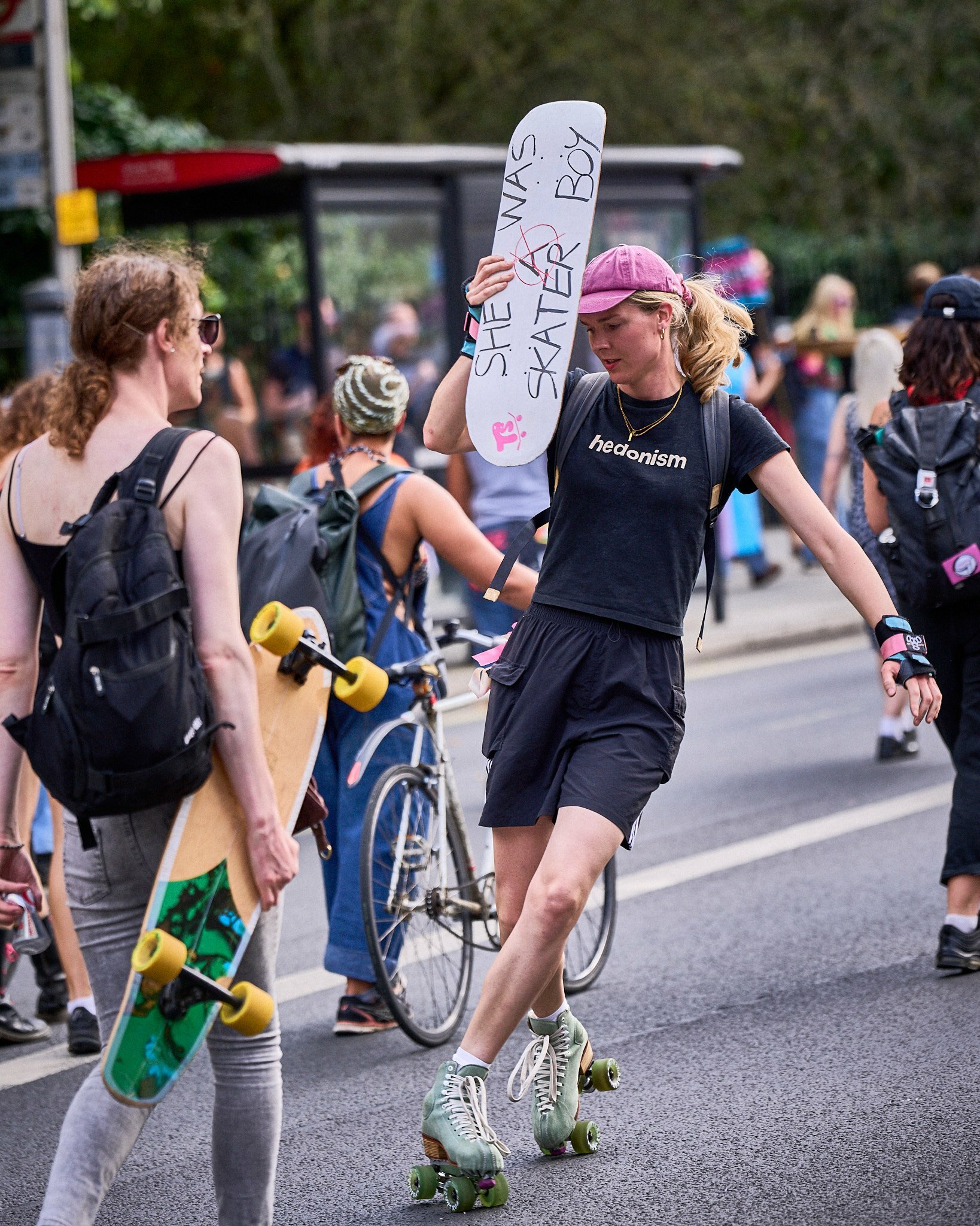 A woman rollerskating holding a skateboard that says 'she was a skater boy'