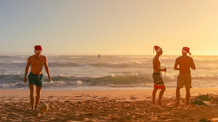 a group of people standing on top of a sandy beach with Christmas hats