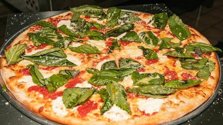 Large margherita pizza with basil and mozzarella sitting on a steel counter