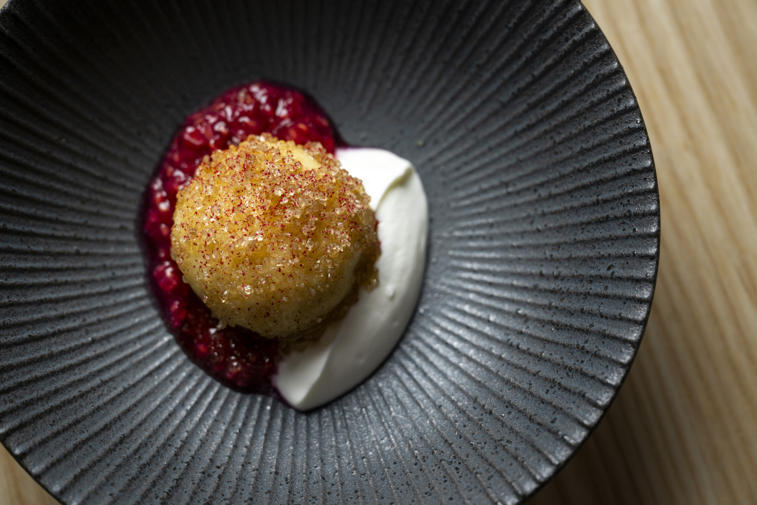 Knedle dessert , a mochiko fried dessert with raspberry and sour cream on a black palte