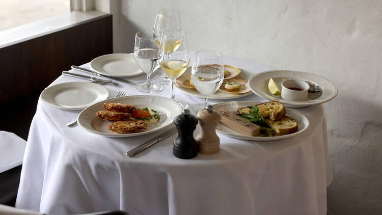 White-clothed table laden with dishes, glasses of wine and salt and pepper.