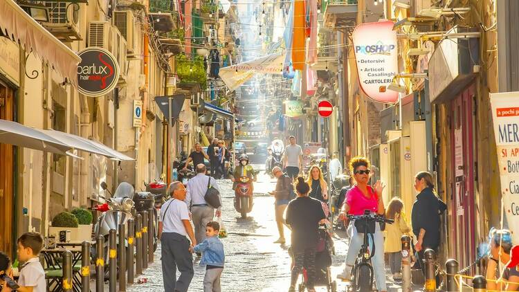 Naples, Italy - 10 June, 2022: Sunny narrow street in Napoli old town, colorful Spagnoli (Spanish) quarter. Italian busy city life in Naples city, people walking down the street.