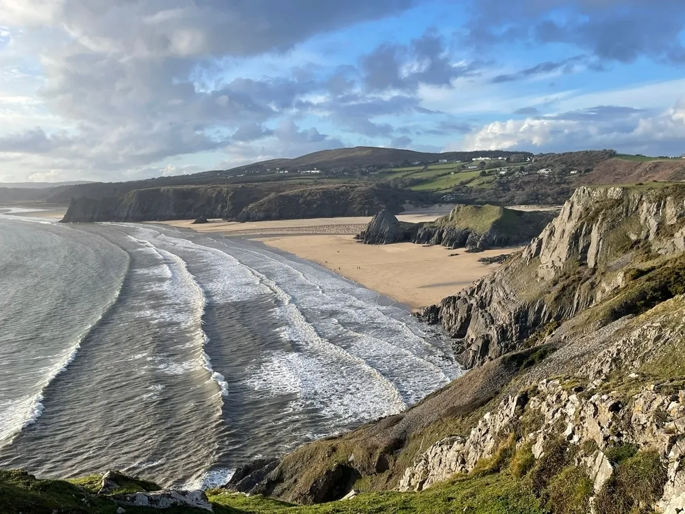 Waves crash onto the beach of Three Cliffs Bay in Wales.