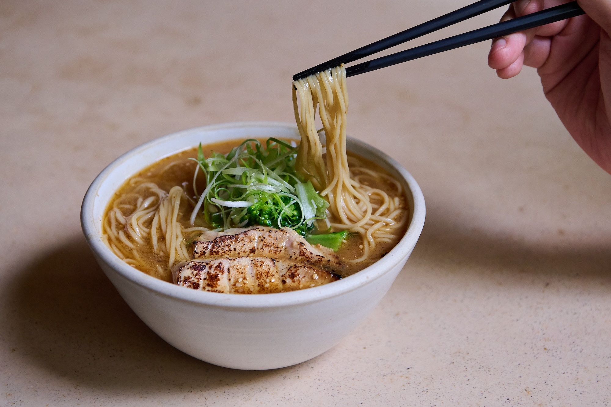 Bowl of ramen in a white bowl with a person hold black chopsticks