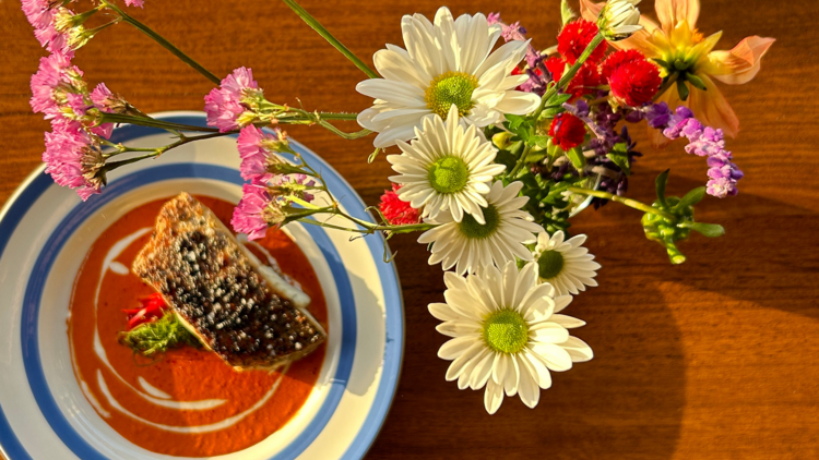 Vibrant fish dish next to a vase of flowers.