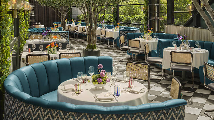 Blue tufted booths and white table clothed tables among greenery and a black and white tiled floor