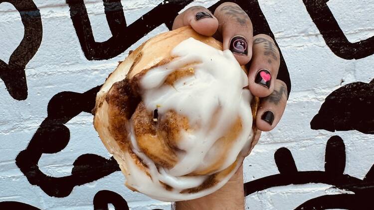 Hand holding a cinnamon bun in front of a black and white grafitti wall