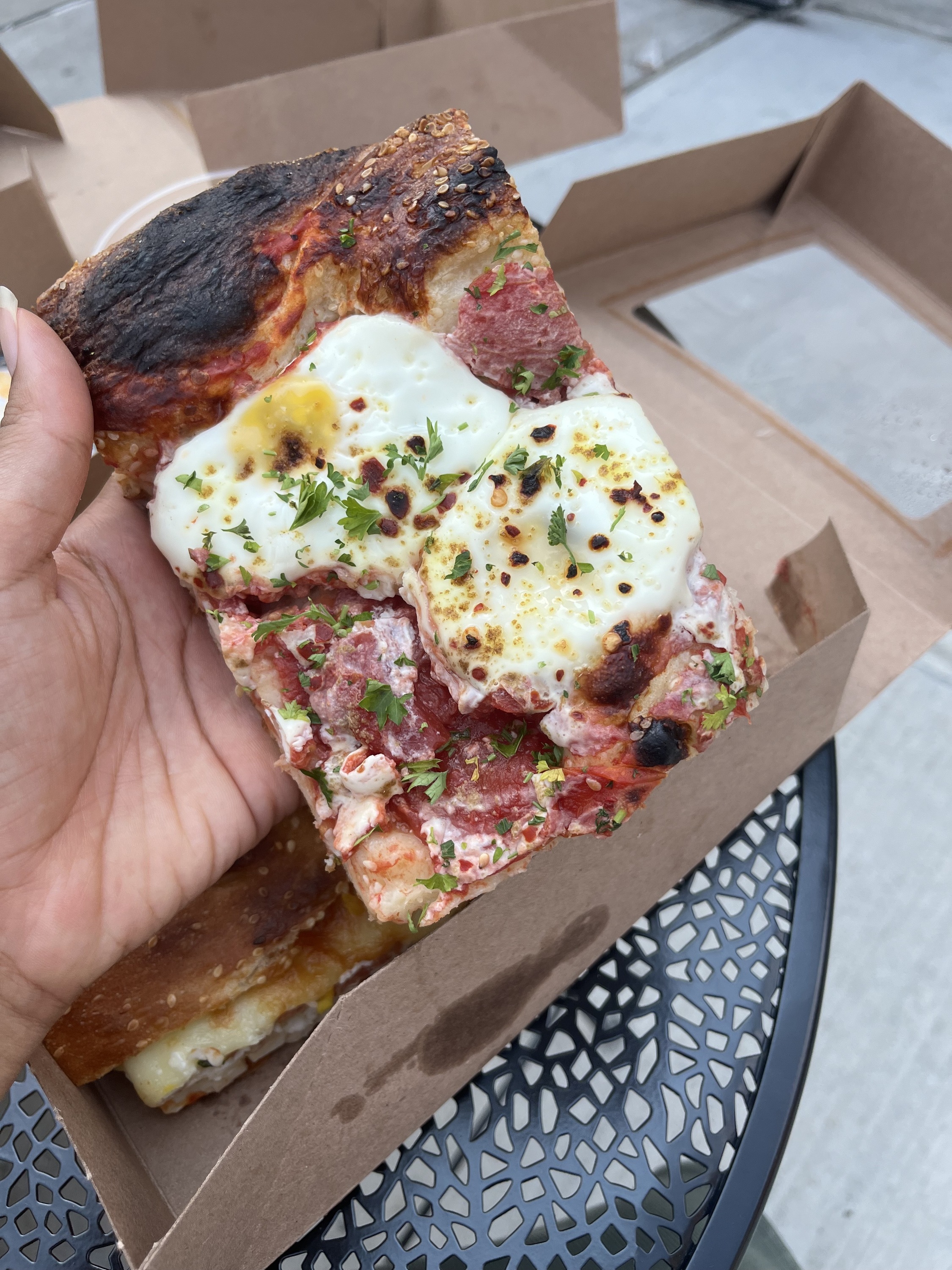 A hand holds the Shakshuka Bread with black table in the background