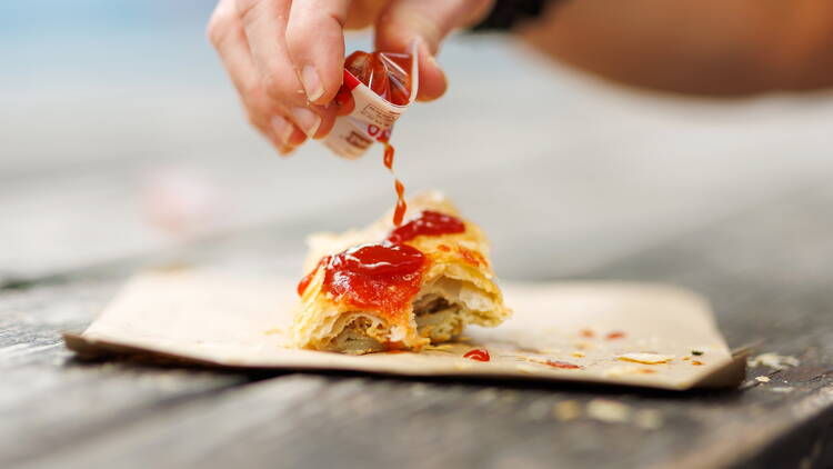 Tomato sauce being squeezed on sausage roll