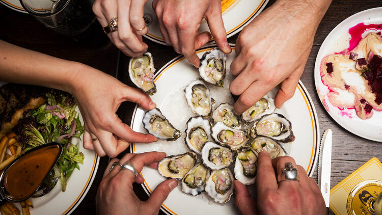 People reaching onto a plate to pick up oysters