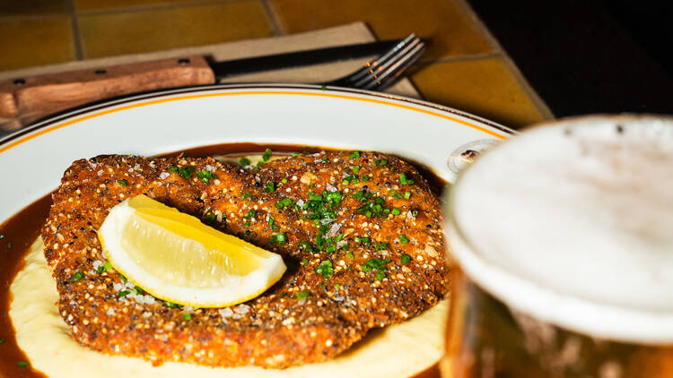 A chicken schnitzel on a plate with lemon, mashed potato and gravy.