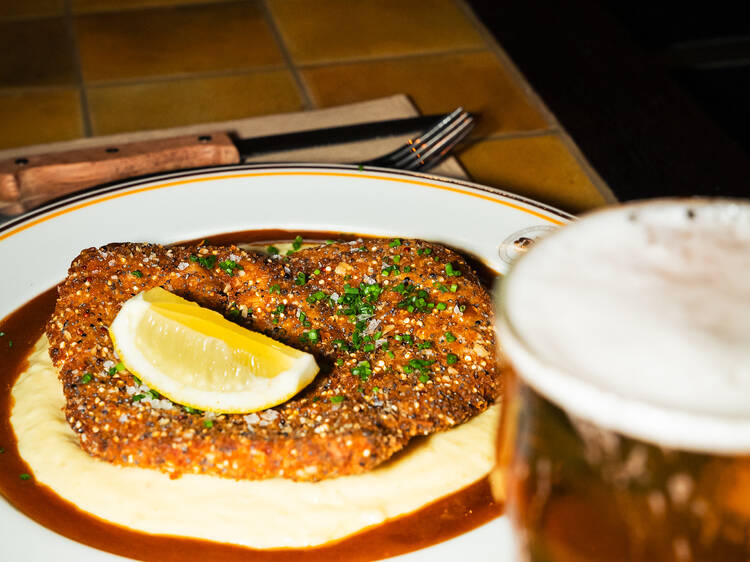 A chicken schnitzel on a plate with lemon, mashed potato and gravy.