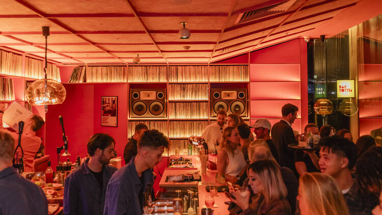 A pink-hued bar packed with people.