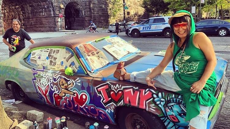 Two people stand next to a car covered in graffiti.