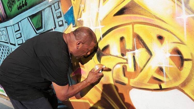 A man paints a golden color on graffiti