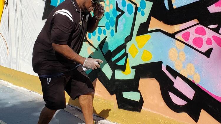 A man paints blue graffiti lettering.