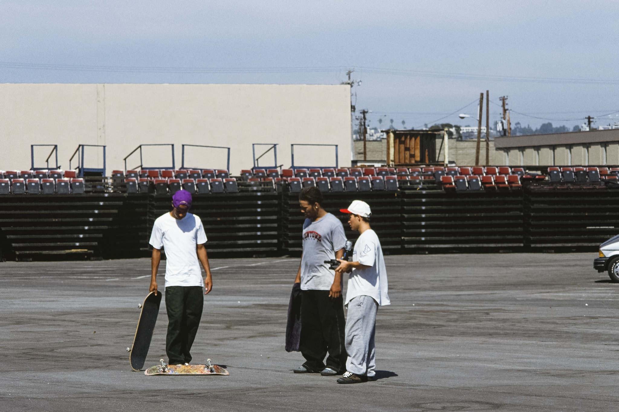 Three men with skateboards on a pavement lot.