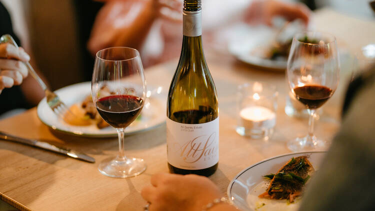 A bottle of red win with glasses on a table.