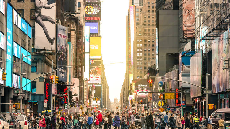 Crowd of people walking across the street in Times Square at sunset