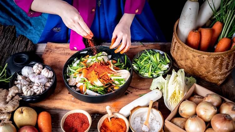 Korean woman is wearing a traditional hanbok, she making Kimchi which is a fermented food preservation of Korean people consisting of many fresh vegetables and fruits, to food concept.