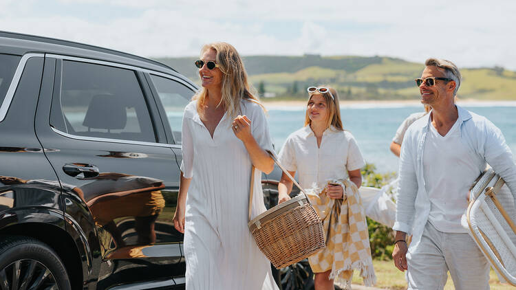 A family walking beside a car with a picnic basket