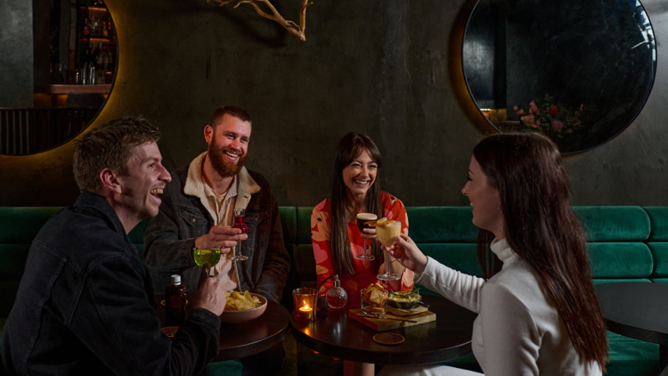 Group of friends enjoying drink in the plush green seats at Bar Clara.