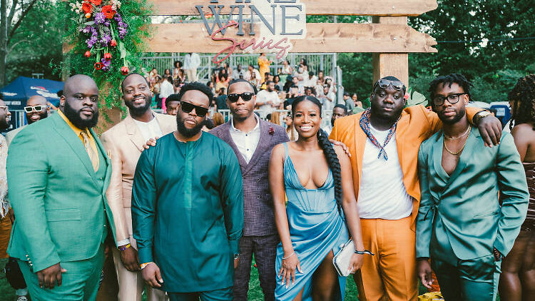 Seven people standing outside in front of a wooden sign that says "Fine Wine Series"