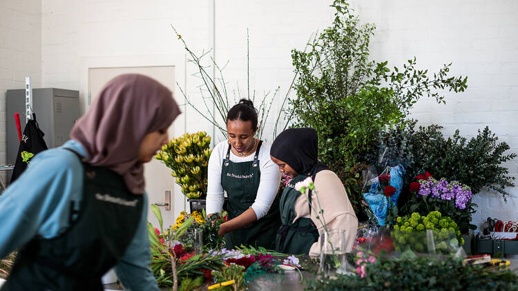 Women working in a florist in a room filled with colourful flowers.