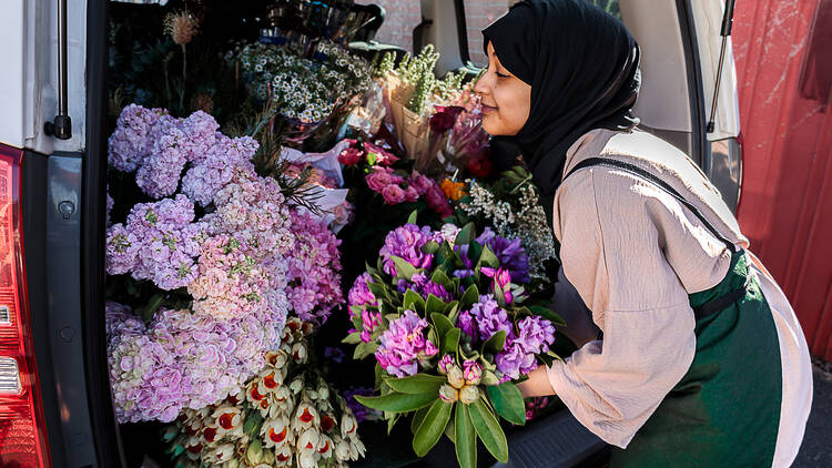 A woman putting colourful bunches of flowers in the back of a car.