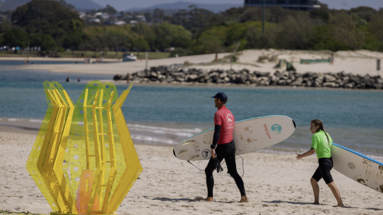 Outdoor sculpture on beach with surfers next to it