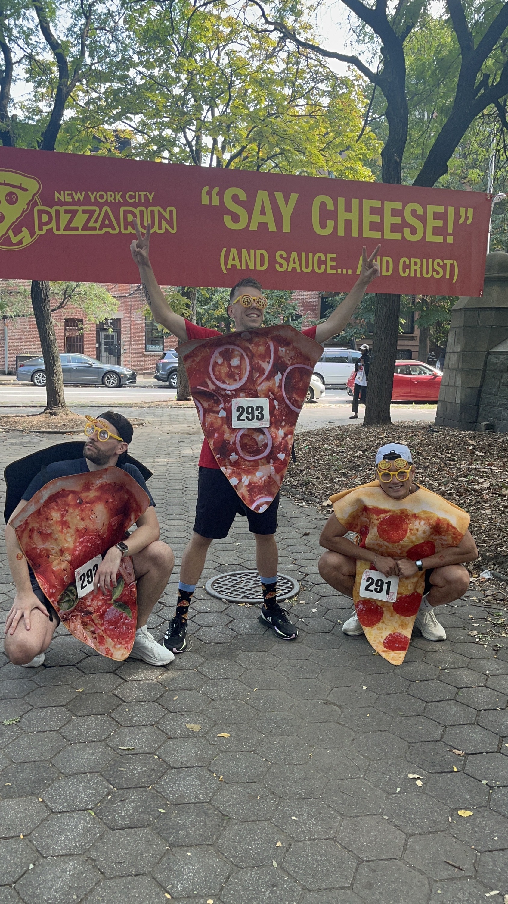 Three men standing in front of banner that reads "Say Cheese (And Sauce...And Crust)"