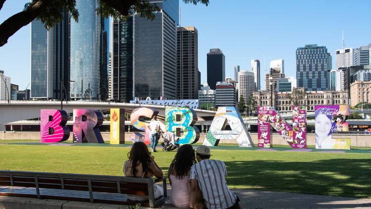 People relaxing on the grass near the Brisbane Sign, with the Brisbane skyline in the background