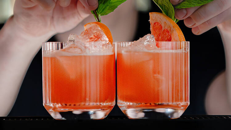 Bartender garnishing two Pink Tutu cocktails at the bar.