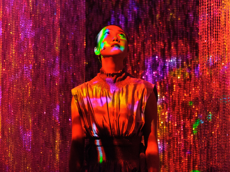 A person under colourful lights in between a sparkly curtain