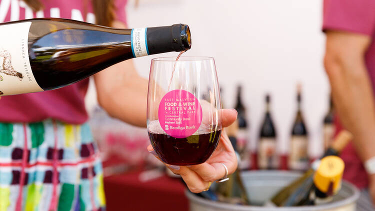 Server pouring red wine into a branded cup.