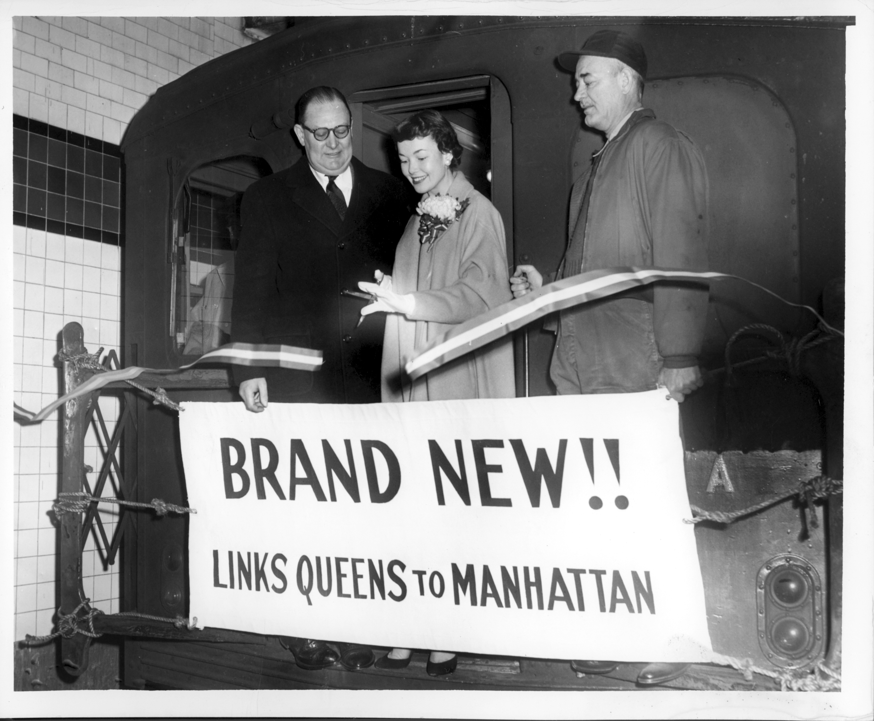 People on a train car with a sign reading Brand New!! Links Queens to Manhattan.