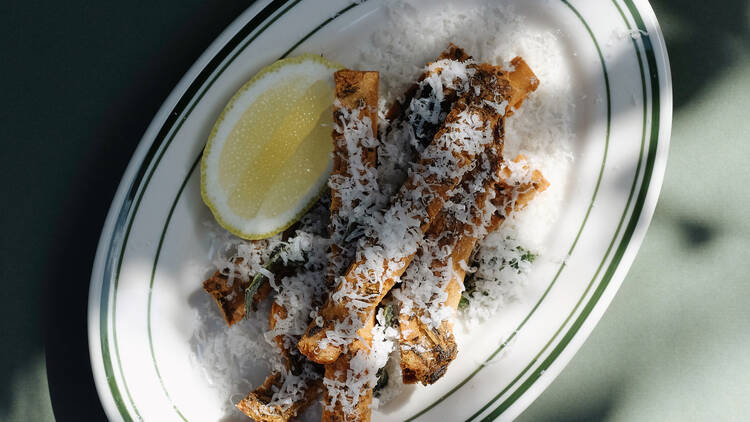 A plate of panisse with cheese and a wedge of lemon.