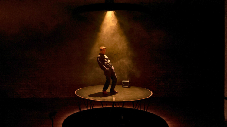 Nicci Wilks stands on a circular stage under a warm toned spotlight