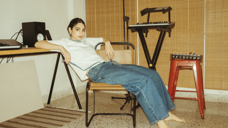 Artist Kavya lounging on a chair in a music room