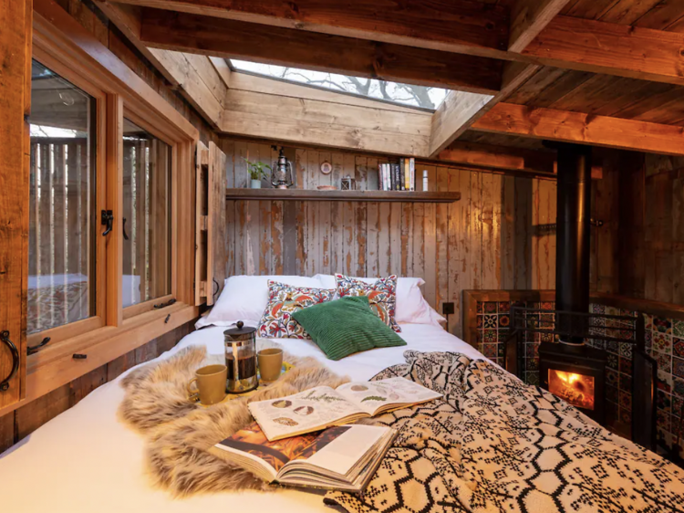 Bedroom in cabin with a skylight, fireplace and a bed with covered with throw and a couple of magazines.