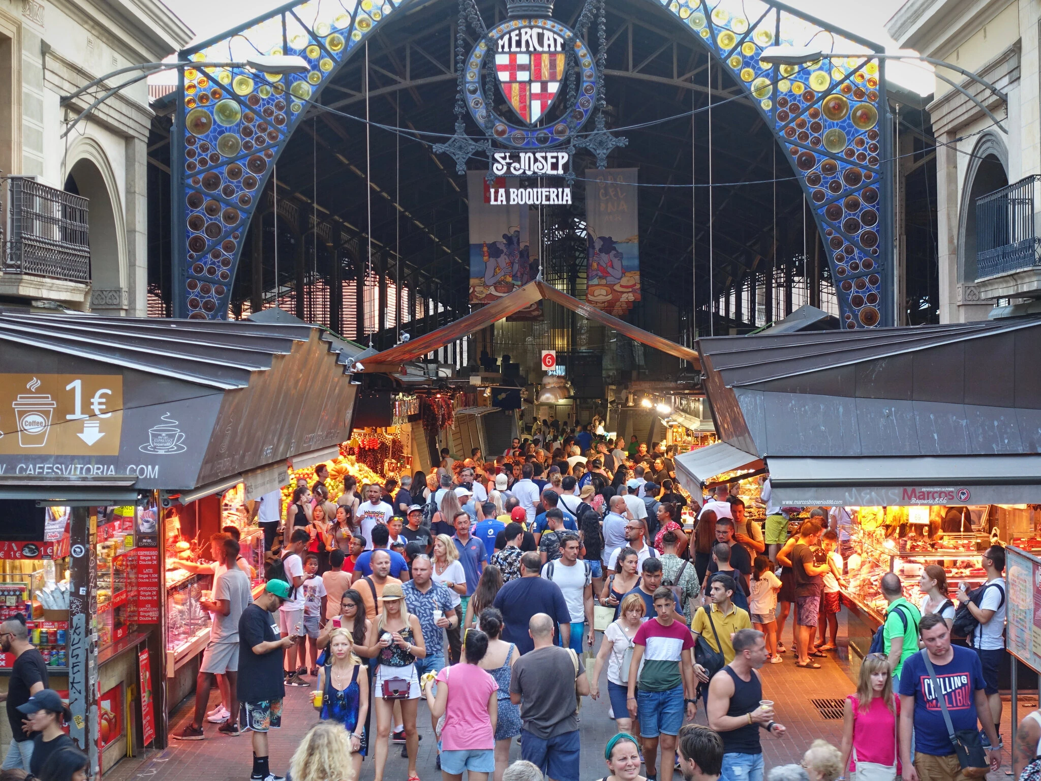 Entrance to La Boqueria market in Barcelona, with crowds walking in and out and market stalls to the sides