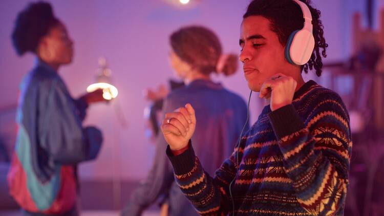 Waist up portrait of ethnic young man dancing with headphones on while enjoying silent disco party in neon light, copy space