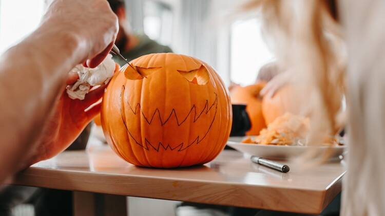 Person using a knife to carve a face design into a pumpkin in preparation for Halloween, pumpkin carving workshop