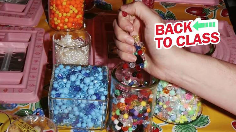 A hand holding colorful beads above a table.