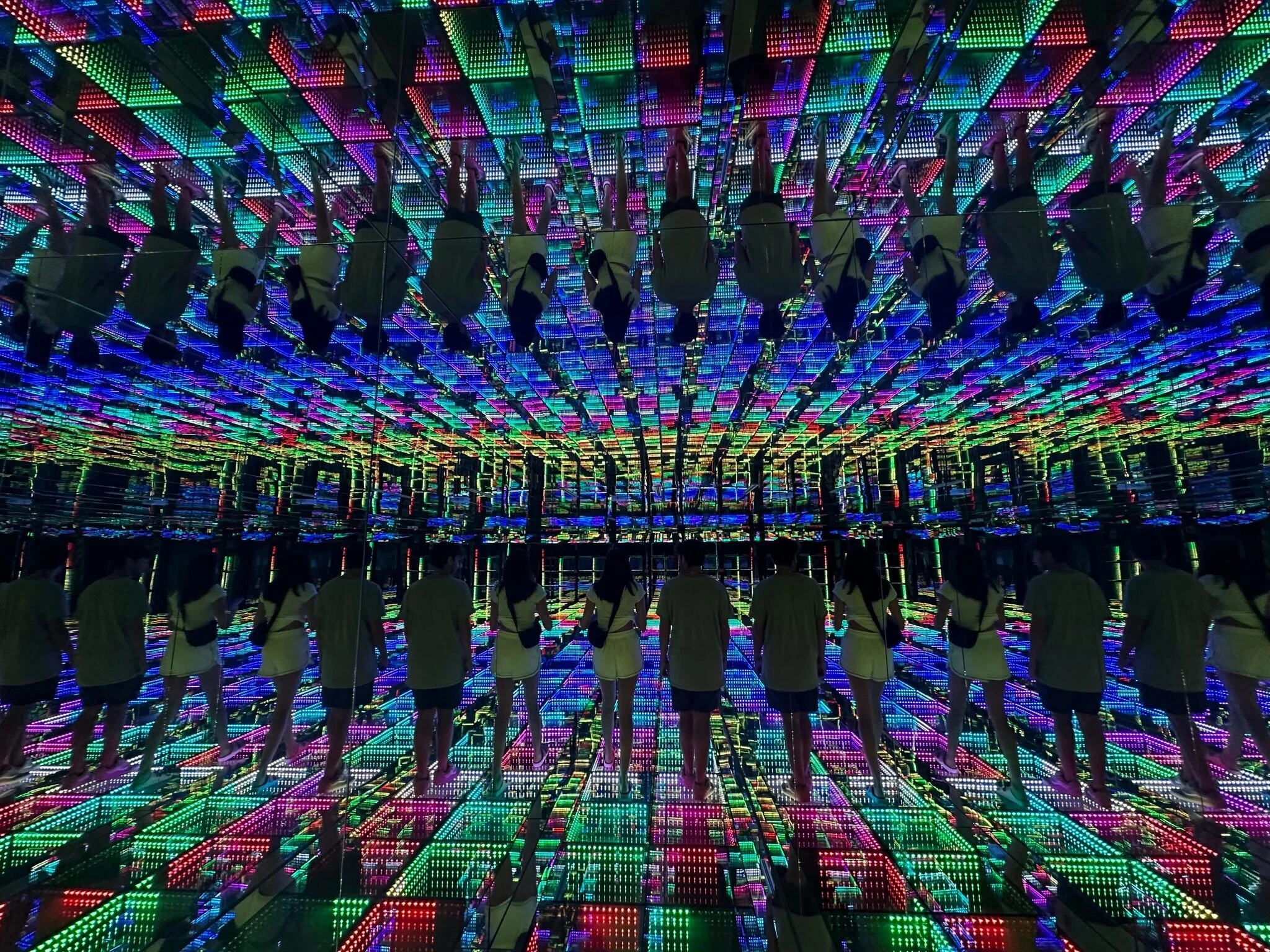 a couple walks on a floor covered in LED lights and are reflected in a series of infinity mirrors so that they are multiplied many times over