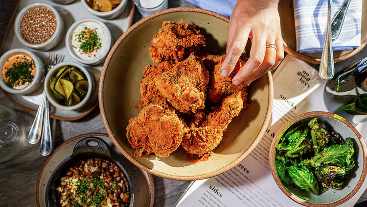 A person's hand reaching for fried chicken on a table.