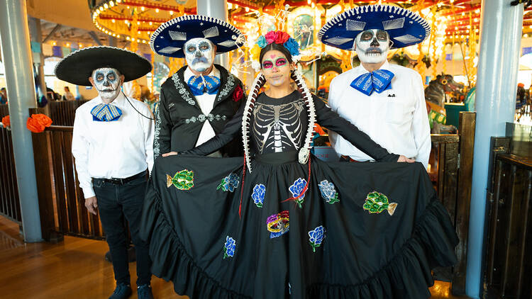 Mariachi singers with faces painted for Dia de los Muertos pose in front of the carousel at the Santa Monica Pier.