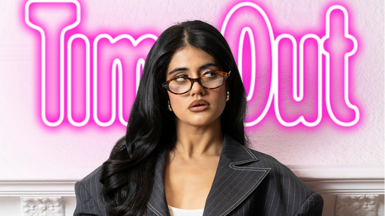 Ayesha Madon wearing glasses, with a Time Out logo behind her