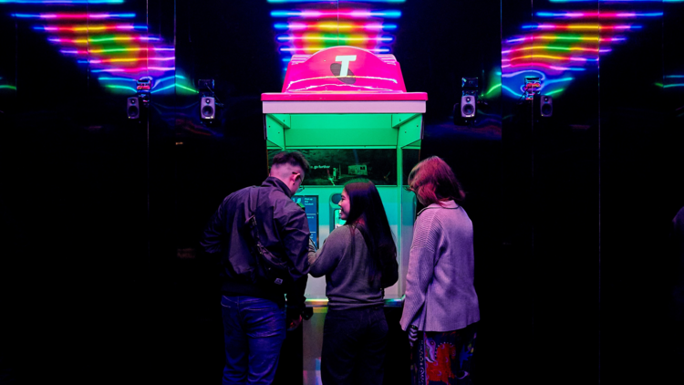 People gather around an illuminated Telstra phone box