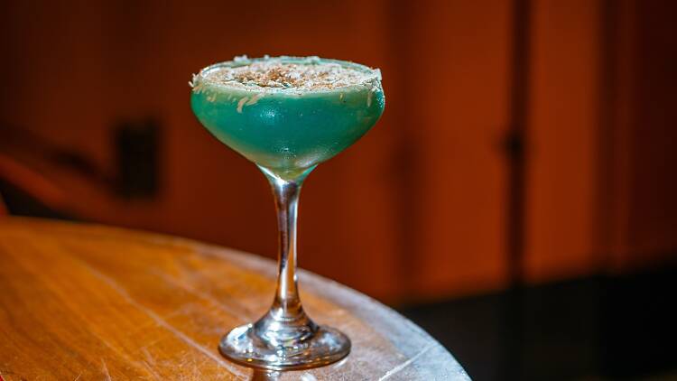 A blue cocktail in a coupe glass with coconut on the rim